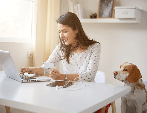 Young Caucasian businesswoman using debit card for online payment with her dog next to her.