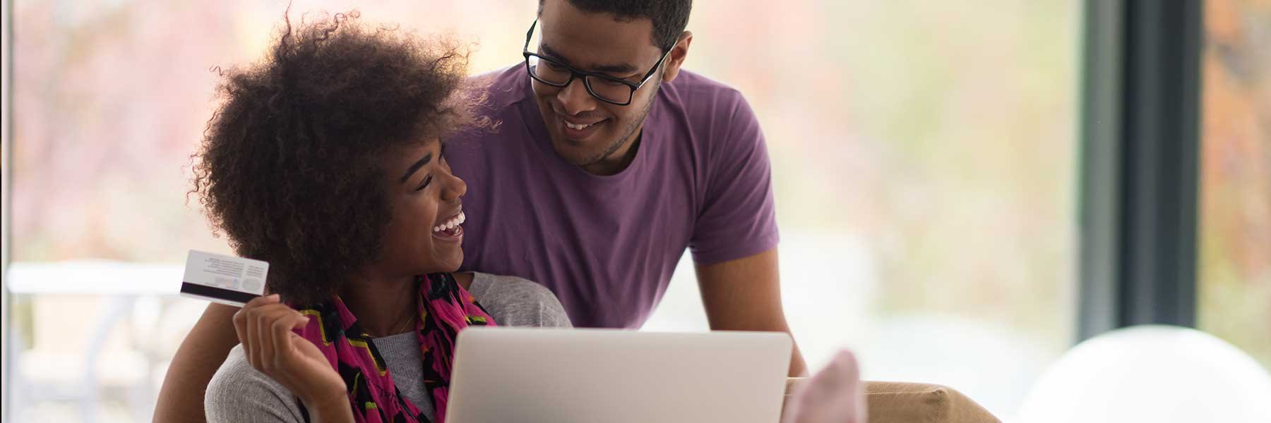 Happy young african american couple shopping online through laptop using debit card at home.